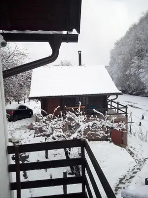 a house covered in snow with a car parked in front at Log Cabins Jovicic in Bosanska Dubica