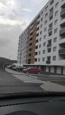 a red car parked in a parking lot next to a large building at M&I Apartment in Doboj