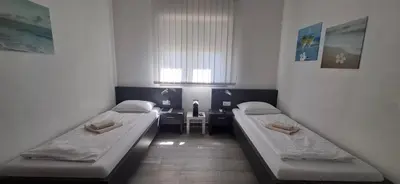 two beds in a room with a table and a window at Gold Apartmani Kozarac in Kozarac