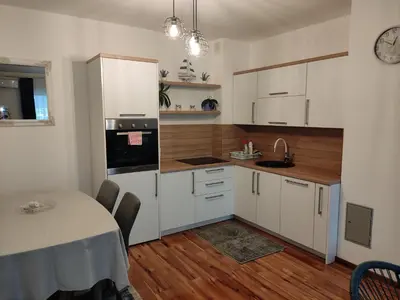 a kitchen with white cabinets and a table and a dining room at Apartman ALEM Bihac in Bihać