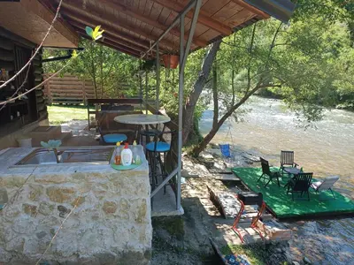 a patio with a table and chairs next to a river at Cottage Auto Camp Vinac in Jajce