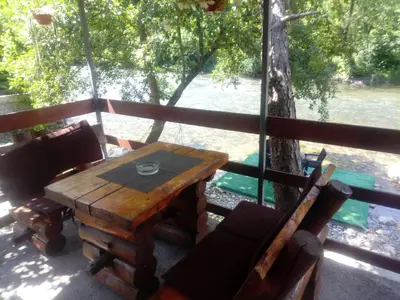 a wooden table and chairs on a porch with a tree at Cottage Auto Camp Vinac in Jajce
