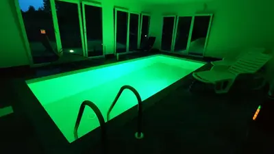 a pool with green lighting in a room with a chair at Beverly Hills SPA Pool House in Donji Podgradci