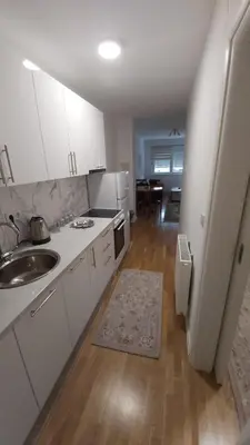 a kitchen with white cabinets and a sink and a table at Mercy Deluxapartment in Visoko