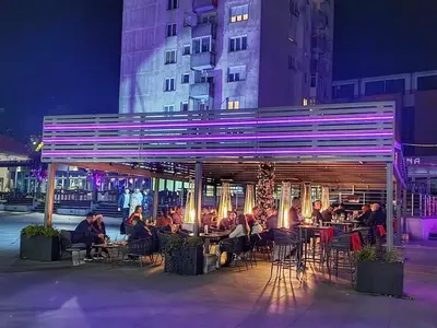 a group of people sitting at tables in front of a building at Apartman City in Livno