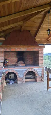 a brick pizza oven under a wooden roof at Vikendica Fenix in Banja Luka