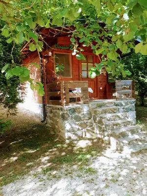 a log cabin under a tree with a stone wall at Vikendice Bungalovi Menzil in Zavidovići