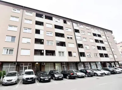 a large building with cars parked in a parking lot at Apartman Garden in Banja Luka