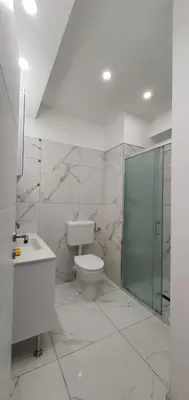 a white bathroom with a toilet and a glass shower at Apartmani Gandi in Bihać