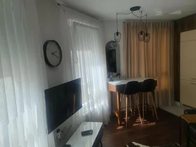 a living room with a clock on the wall and a table at Tuzla Trg - Tuzla Square in Tuzla