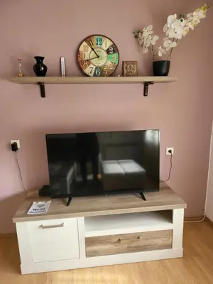 a television on a stand with a clock on a wall at Stan u centru Prnjavor in Prnjavor