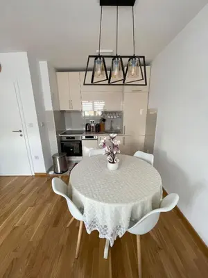 a dining room table with white chairs and a kitchen at Orhidea Doboj in Doboj
