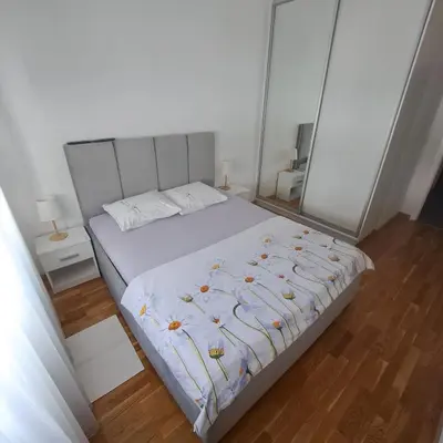 a bedroom with a white bed and a wooden floor at Apartman LUAN in Banja Luka