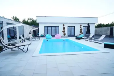 a swimming pool on a patio with chairs and a house at Villa Vidovic Banja Luka in Banja Luka