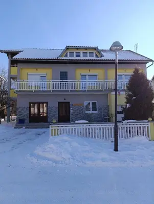 a yellow house with a white fence in the snow at Apartman Ivano in Kupres
