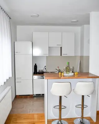 a kitchen with white cabinets and two bar stools at Apartman Giljen in Teslić