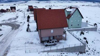 a small house with a car parked in the snow at Apartmani Čiča in Kupres