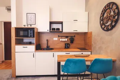 a kitchen with white cabinets and a wooden table and blue chairs at Central Square Apartment in Banja Luka