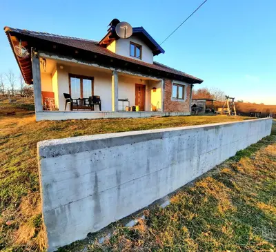 a small house behind a concrete wall at Kuća na dan Vrla strana in Bosansko Petrovo Selo