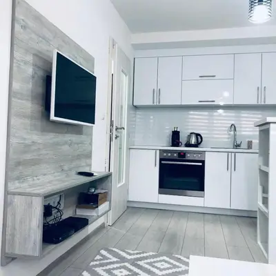 a kitchen with white cabinets and a tv on the wall at Mini apartman Smile Travnik in Travnik
