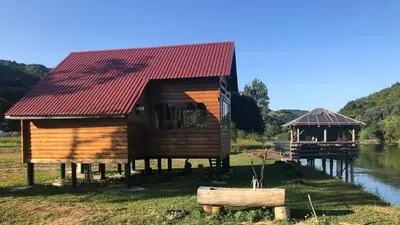 a wooden house with a red roof next to a river at Vikendica Na Plivi in Šipovo