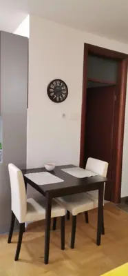 a black dining room table with white chairs and a clock at Apartman Benz studio in Banja Luka
