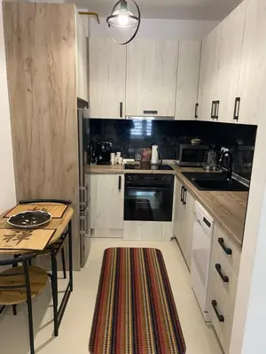 a kitchen with white cabinets and a table with a rug at New Apartment in the City in Visoko