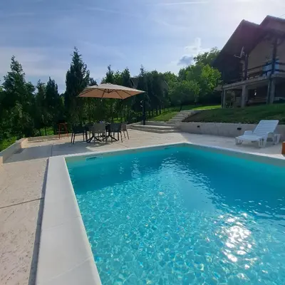 a blue swimming pool with a table and an umbrella at Vikendica Nature park Banja Luka in Banja Luka