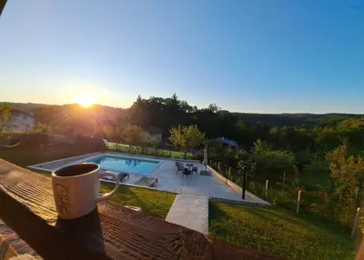 a cup of coffee sitting on a railing with a view of a pool at Vikendica Nature park Banja Luka in Banja Luka
