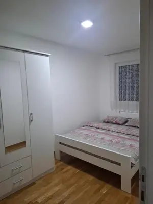 a white bedroom with a bed and a cabinet at Apartman Bulevar in Doboj