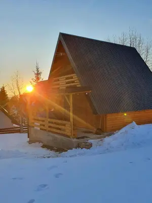 a wooden cabin in the snow with the sun setting at Planinska brvnara in Kupres