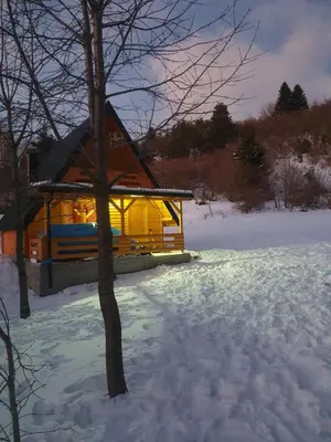 a log cabin with lights on in the snow at Planinska brvnara in Kupres