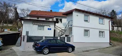 a blue car parked in front of a white house at Apartmani Roki in Tuzla