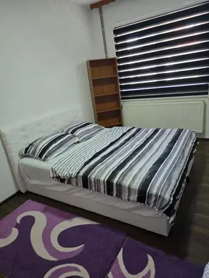a bed in a bedroom with a purple rug and a window at Apartman Vany in Tuzla