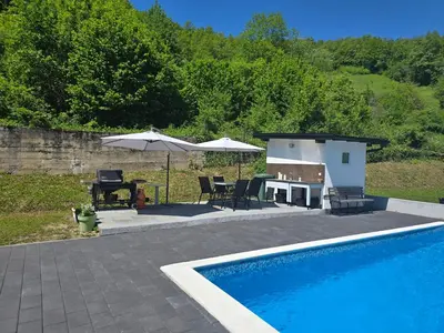 a swimming pool with a table and an umbrella at Vikendica Lohovo in Bihać