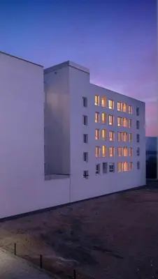 a large white building with illuminated windows at dusk at Apartman Sisters in Sanski most