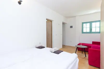 a bedroom with a white bed and a red couch at Retro Village Ravne in Visoko