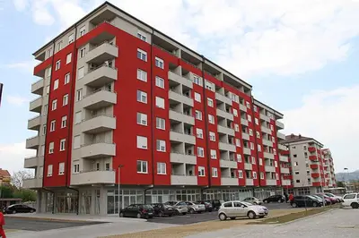 a red building with cars parked in a parking lot at Apartmani Casa in Banja Luka