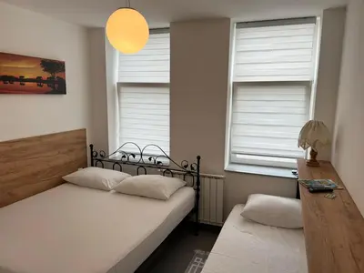 a bedroom with two beds and two windows at Apartmani Aurora in Tuzla