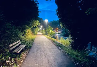 a bench on a path next to a river at night at Motel Platani Kotor Varoš in Kotorište