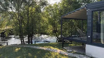 a house with a picnic table next to a river at Waterfall Glamping Cabin in Bihać
