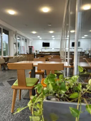 a cafeteria with wooden tables and chairs and plants at Hotel Pilot in Cazin