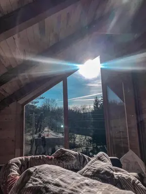 a bed in front of a window with the sun shining through at Vikendica Brvnara Marčetić in Banja Luka