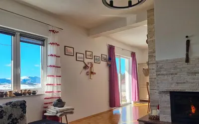 a living room with a fireplace and two windows at Rosa Canina Kupres in Kupres
