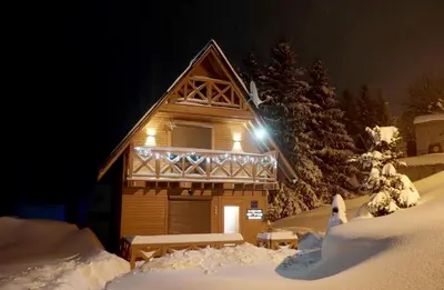 a log cabin in the snow at night at Planinska kuca NATURA in Vlasic