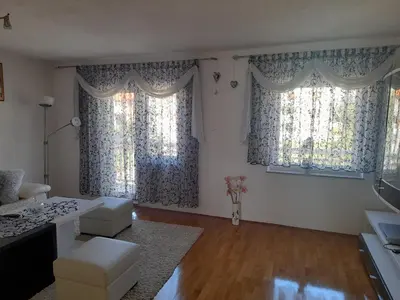 a living room with two large windows with curtains at Apartman Zoran in Livno