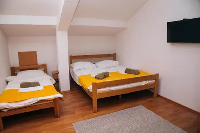 two beds in a room with a tv on the wall at Domaćinska Kuća Banja Luka in Banja Luka