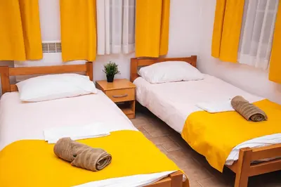 two beds in a room with yellow curtains at Domaćinska Kuća Banja Luka in Banja Luka