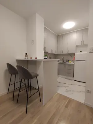 a kitchen with white cabinets and a counter and chairs at Apartman 7 Ladies in Banja Luka