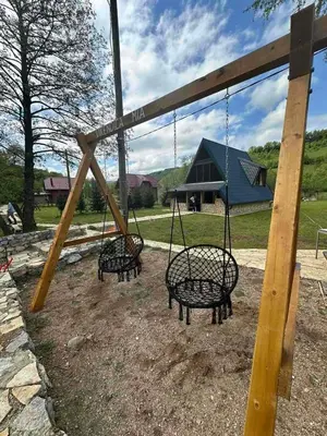 three swings in a playground with a house in the background at Vikendica Mia in Šipovo